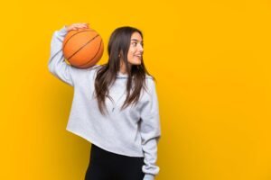 The Elite Sport Mental Health Blog Young woman holding basketball on her shoulder, looking happily to the side